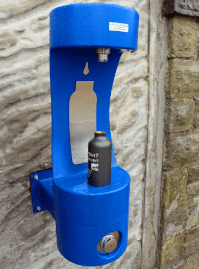 Blue outdoor bottle filler with a bottle on it ready to be refilled.