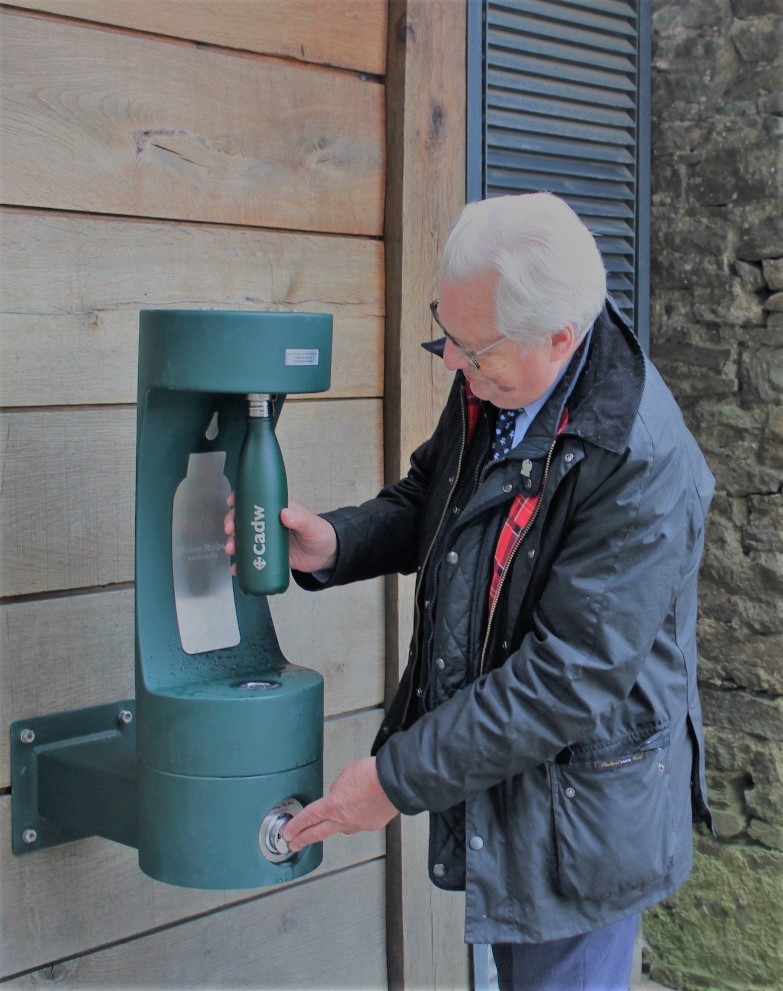 A man refilling his water bottle at a green bottle filler. 