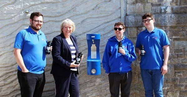 People smiling next to the outdoor bottle refill station. 