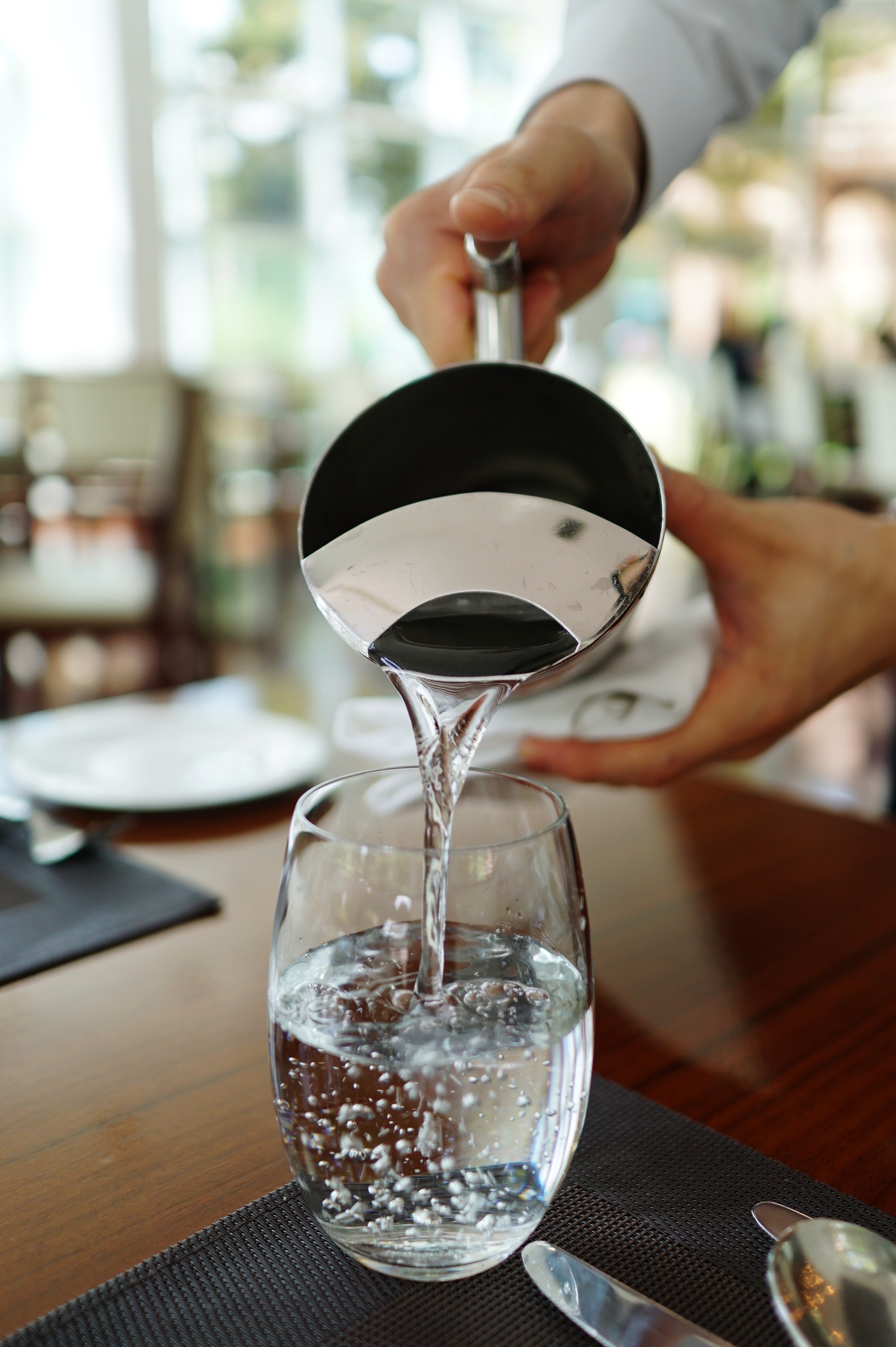 Pouring water into a clear glass from a jug.