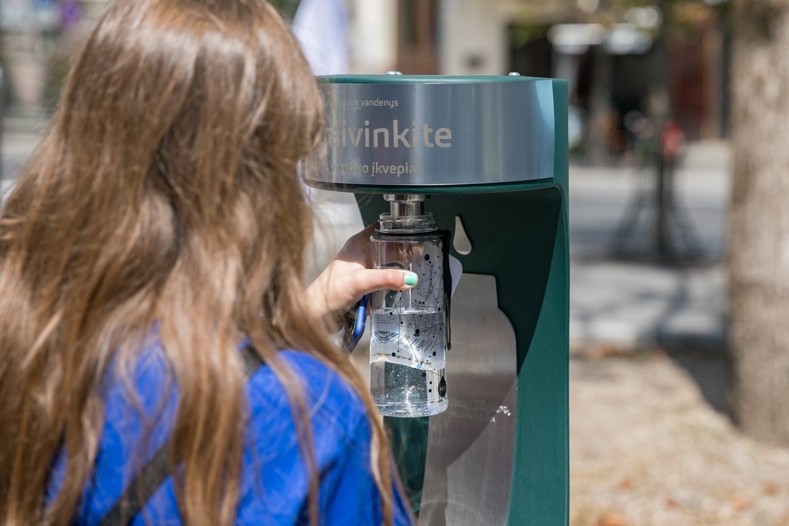 Girl with brown hair refilling her water bottle at the new public drinking fountain in Vilnius, Lithuania