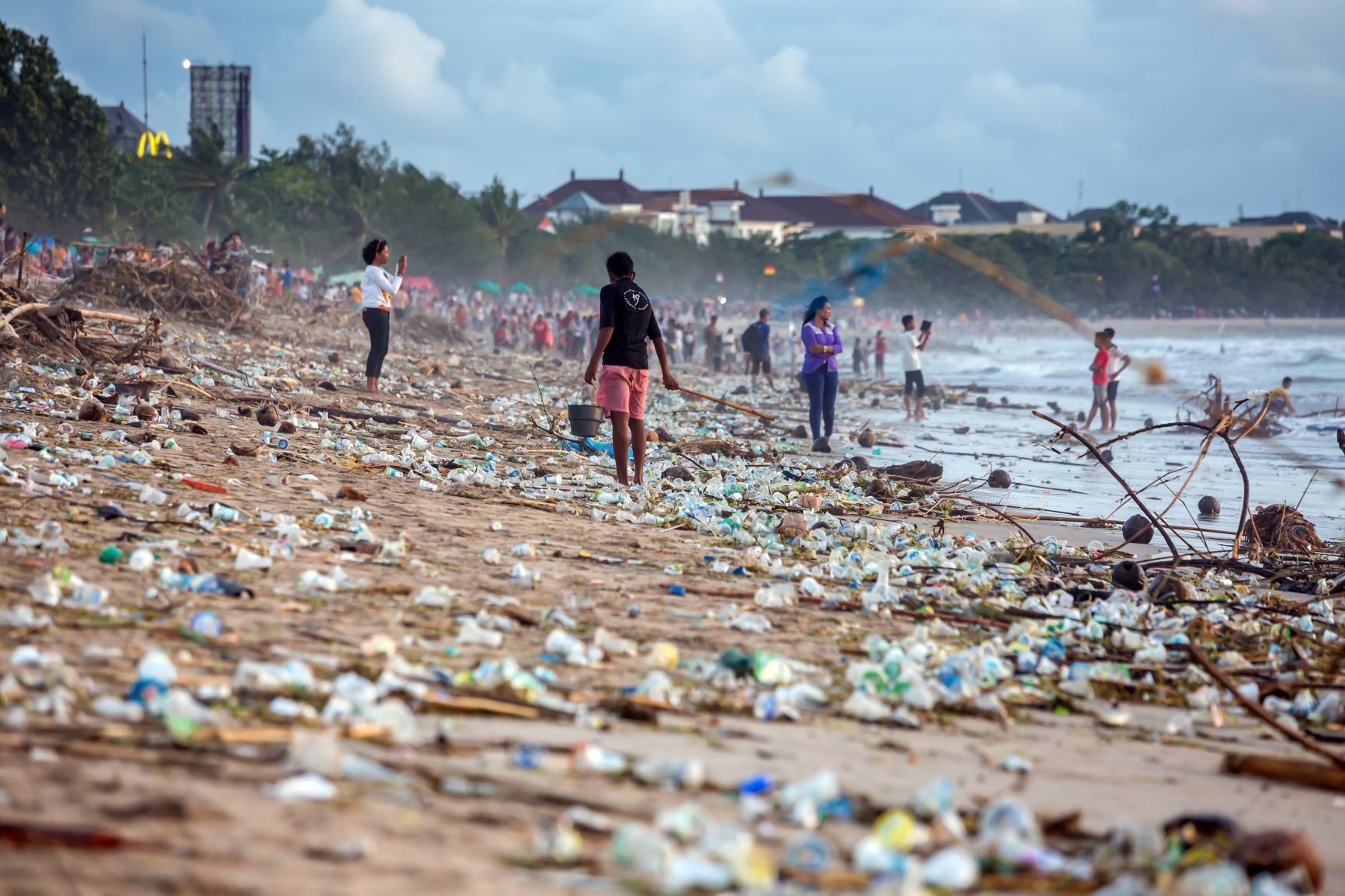 Beach full of plastic waste and people collecting it.