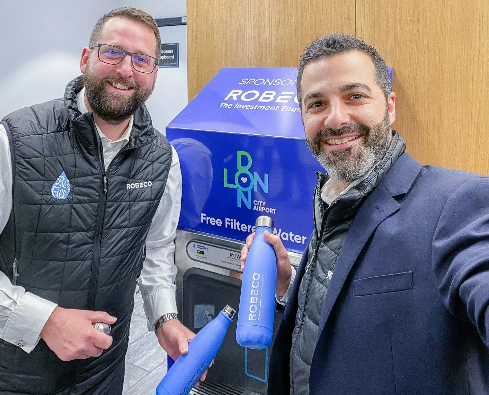 Happy People Refilling From The New Branded Bottle Filling Station At The Airport